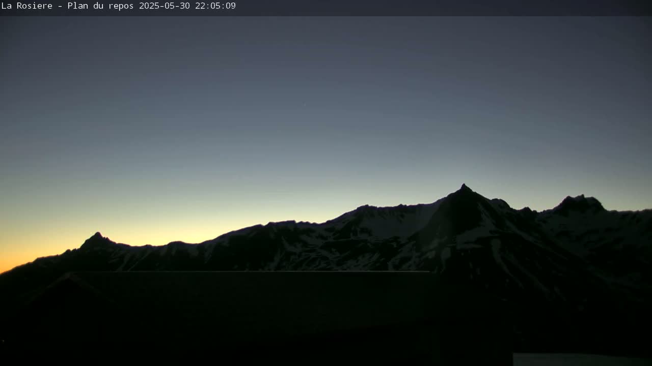 A snow-capped mountain range is silhouetted against a twilight sky.