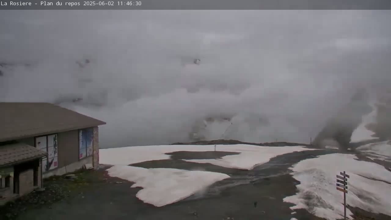 A low-lying building with snow patches on the ground is visible in foggy conditions.