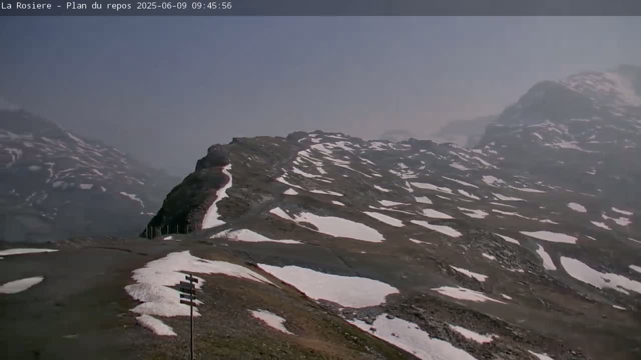 A hazy, mountainous landscape with patches of snow on the ground is visible.