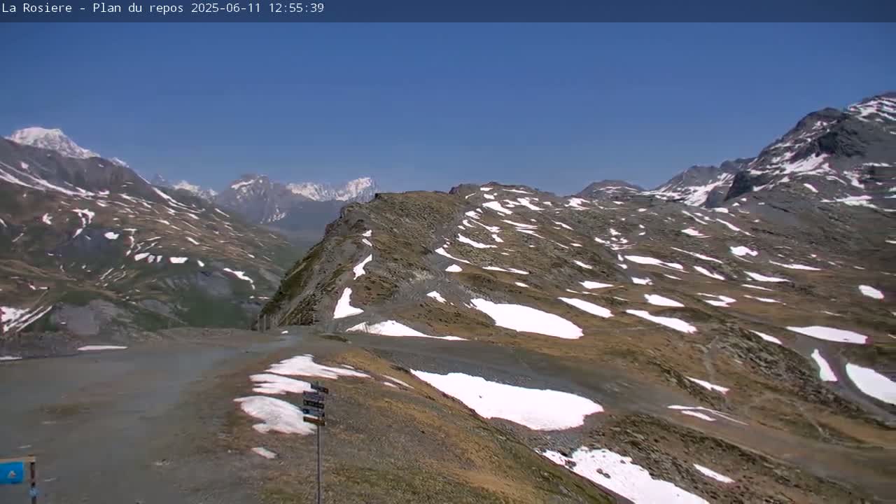 A mountain pass with patches of snow under a clear blue sky.