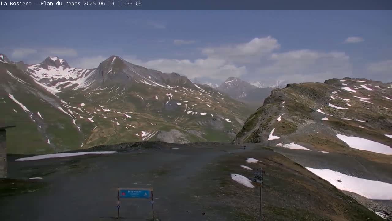 A mountain pass with patches of snow under a partly cloudy sky.