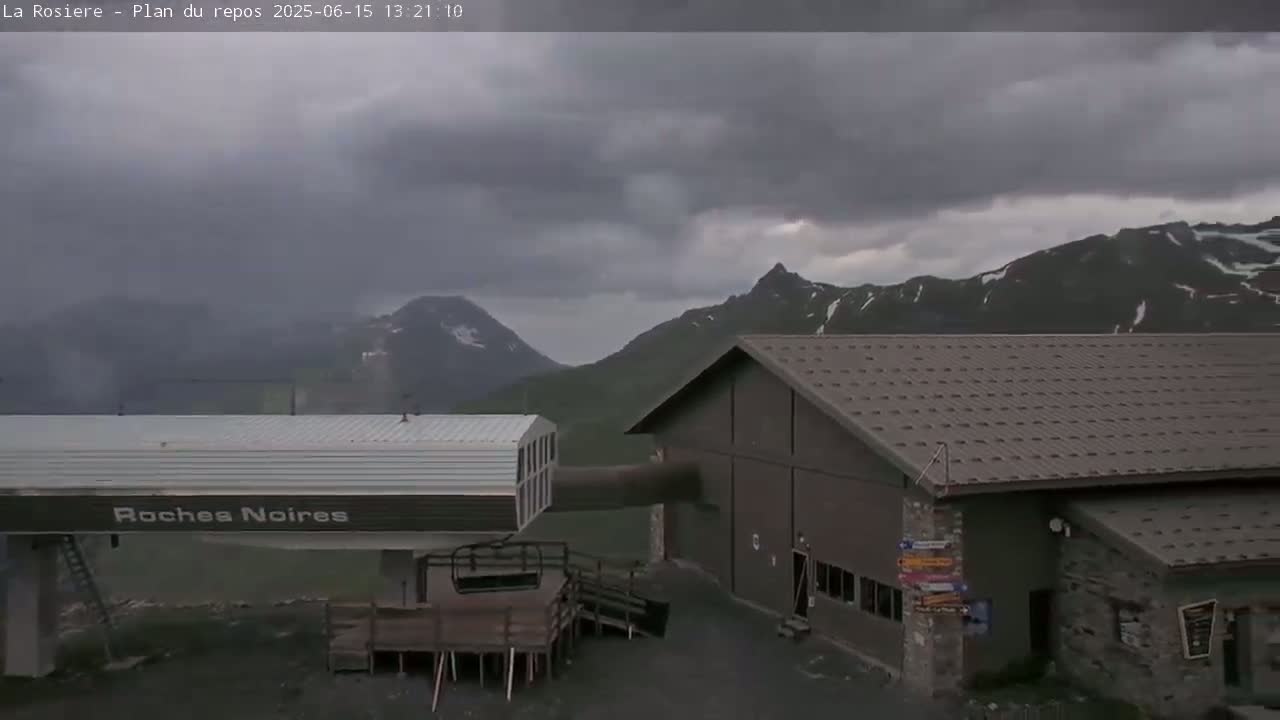 A ski lift station is situated near a mountain range under a cloudy sky.