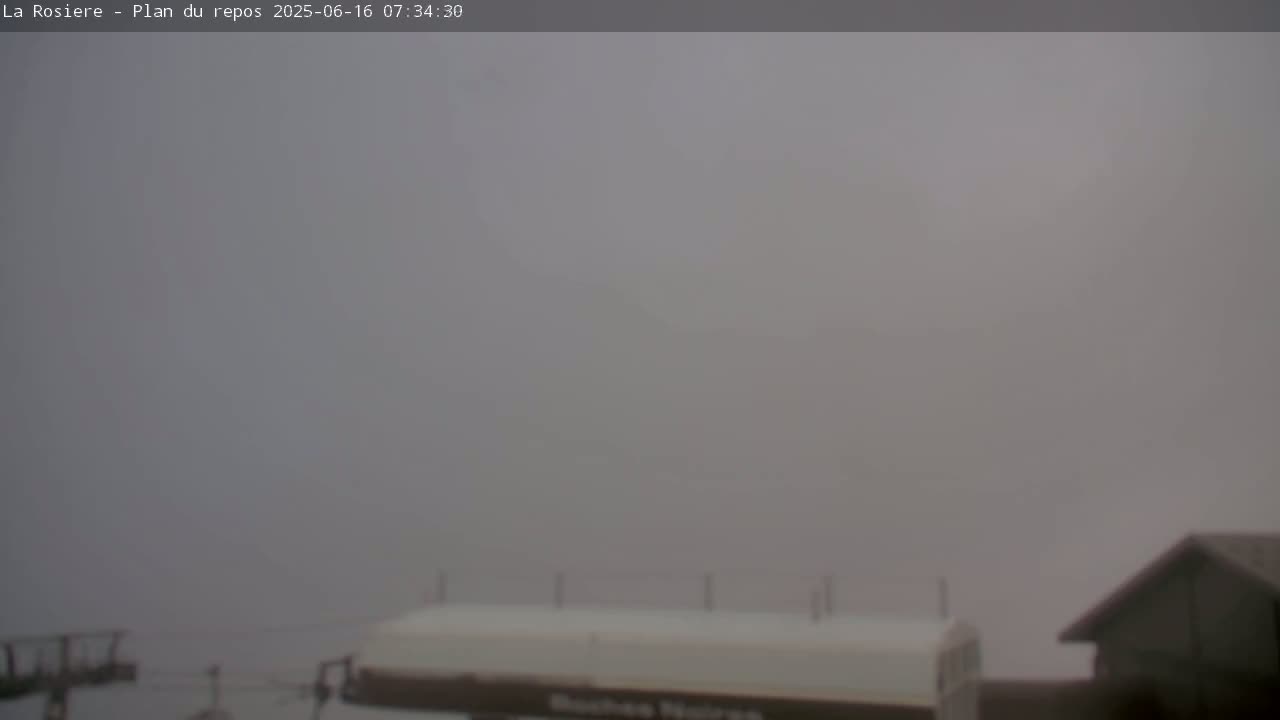 A foggy, outdoor scene shows a portion of a building and some indistinct structures in the hazy distance.