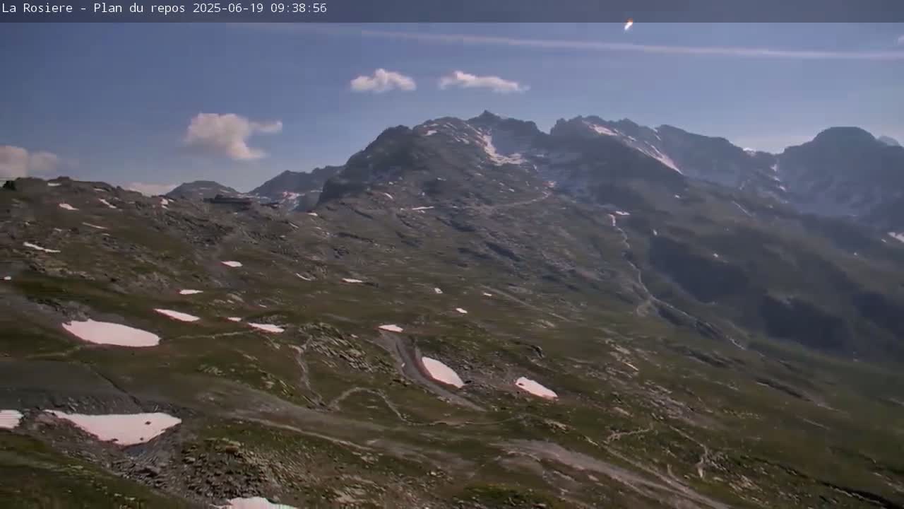 A high-angle view shows a mountainous landscape with patches of snow under a mostly clear blue sky.