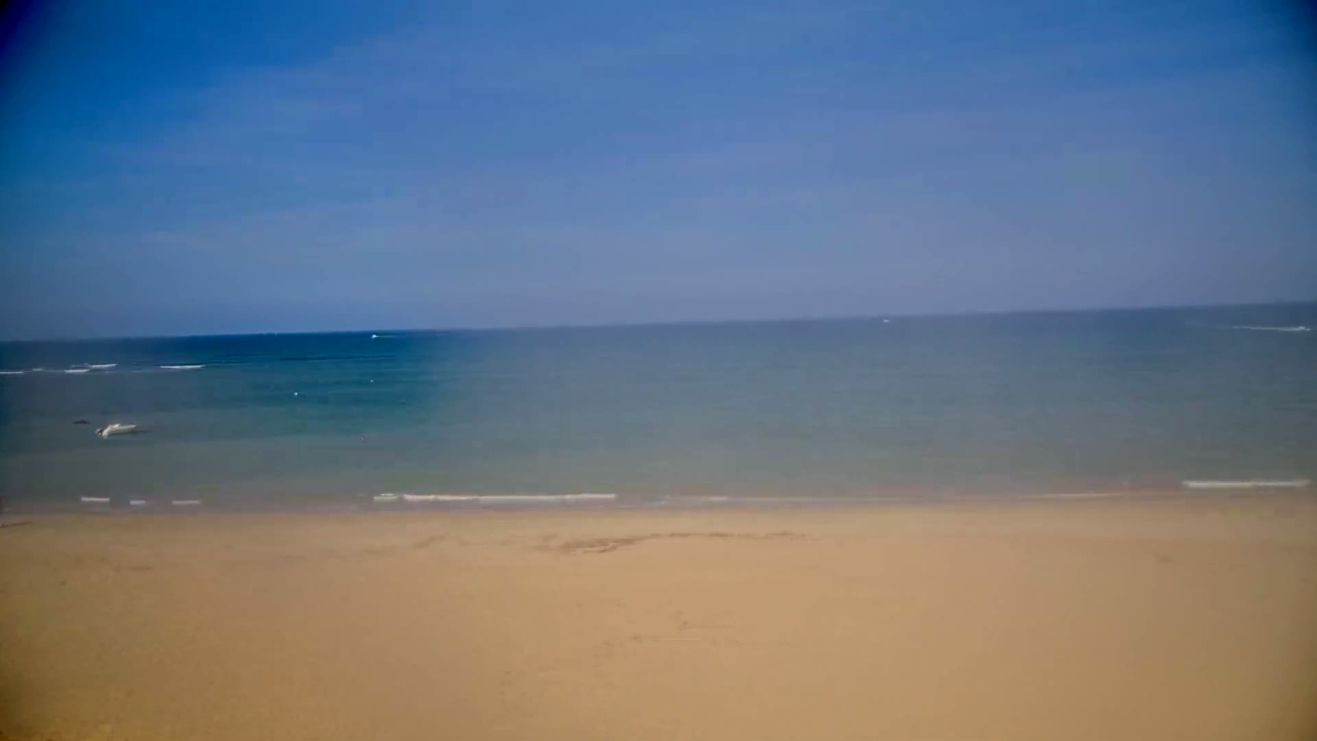 A sandy beach stretches to a calm, blue ocean under a clear sky.