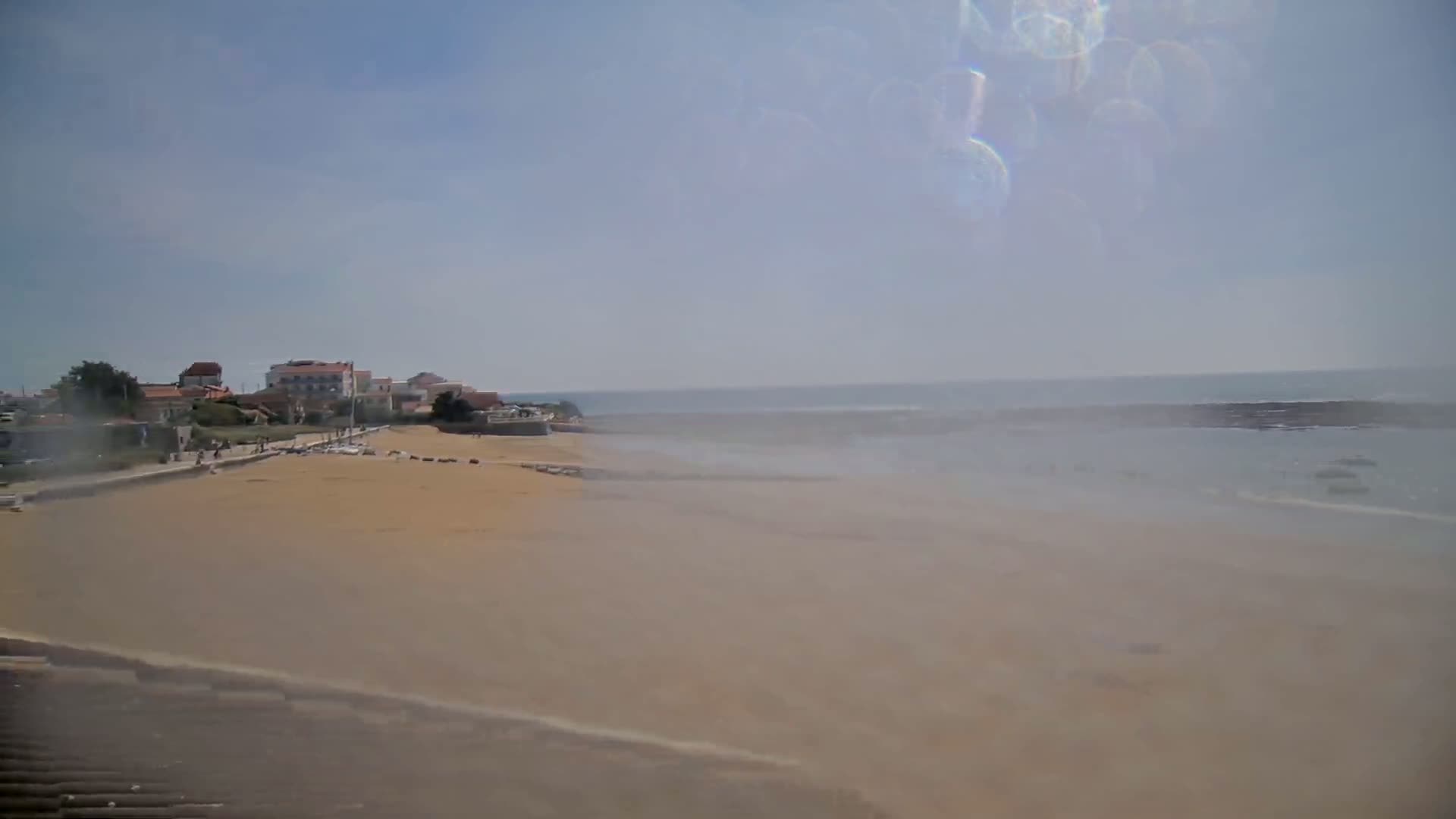 A hazy, sunny day reveals a sandy beach stretching to a calm ocean, with a small town visible in the background.