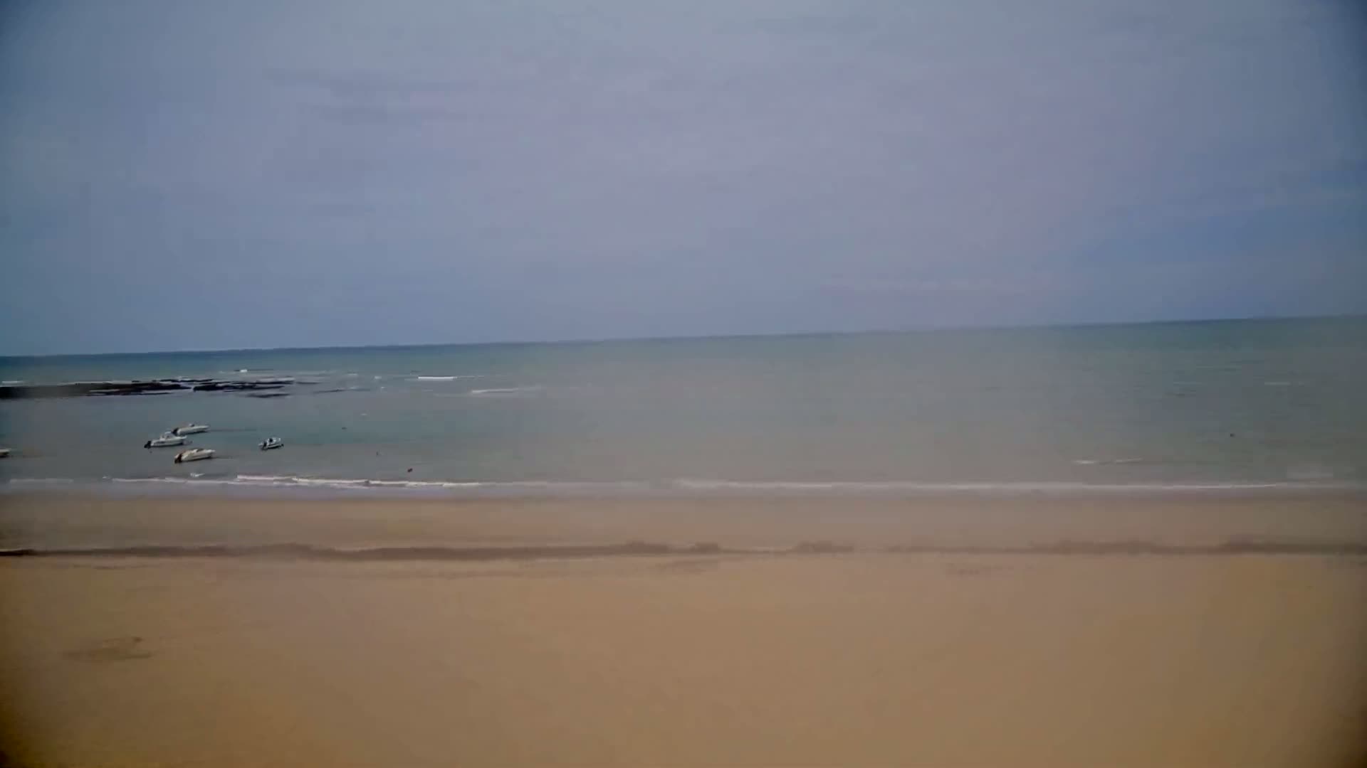 A wide, sandy beach stretches to a calm, gray-blue ocean under an overcast sky.