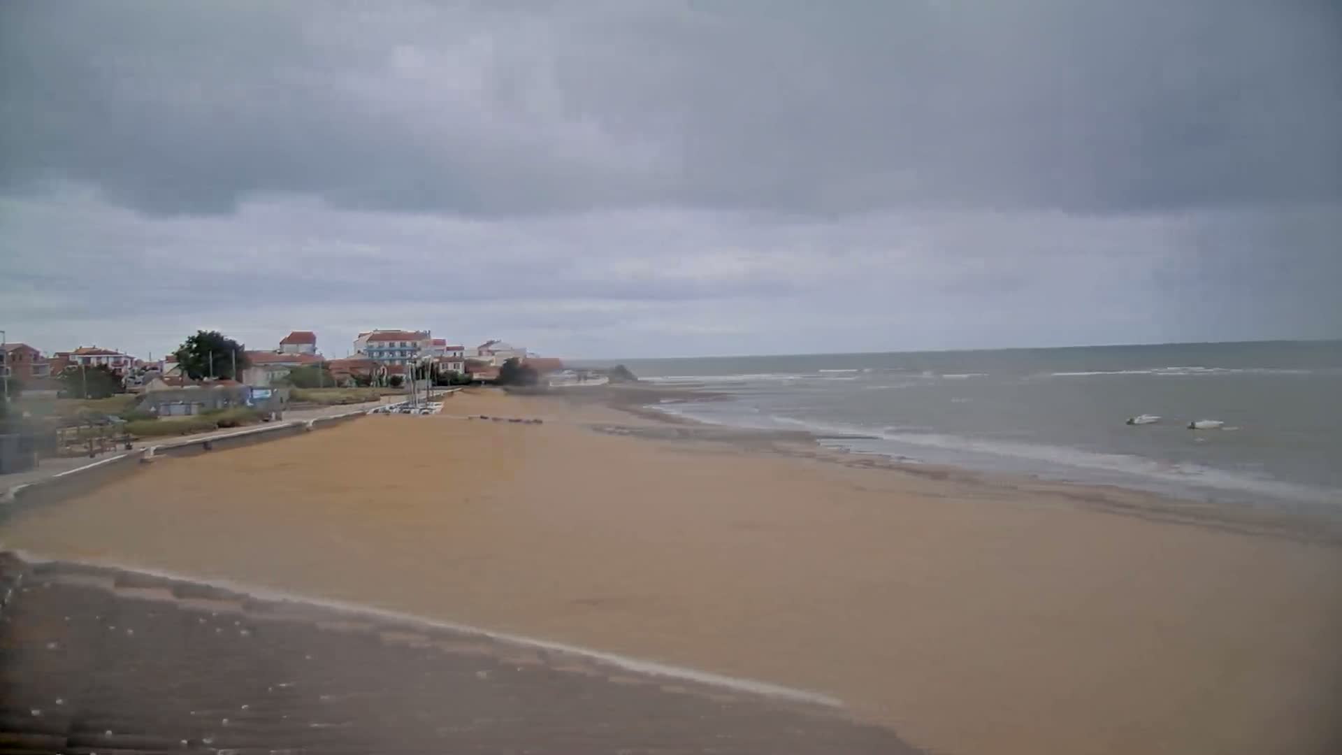 A sandy beach stretches out to a calm, grey sea under an overcast sky, with a small town visible in the background.
