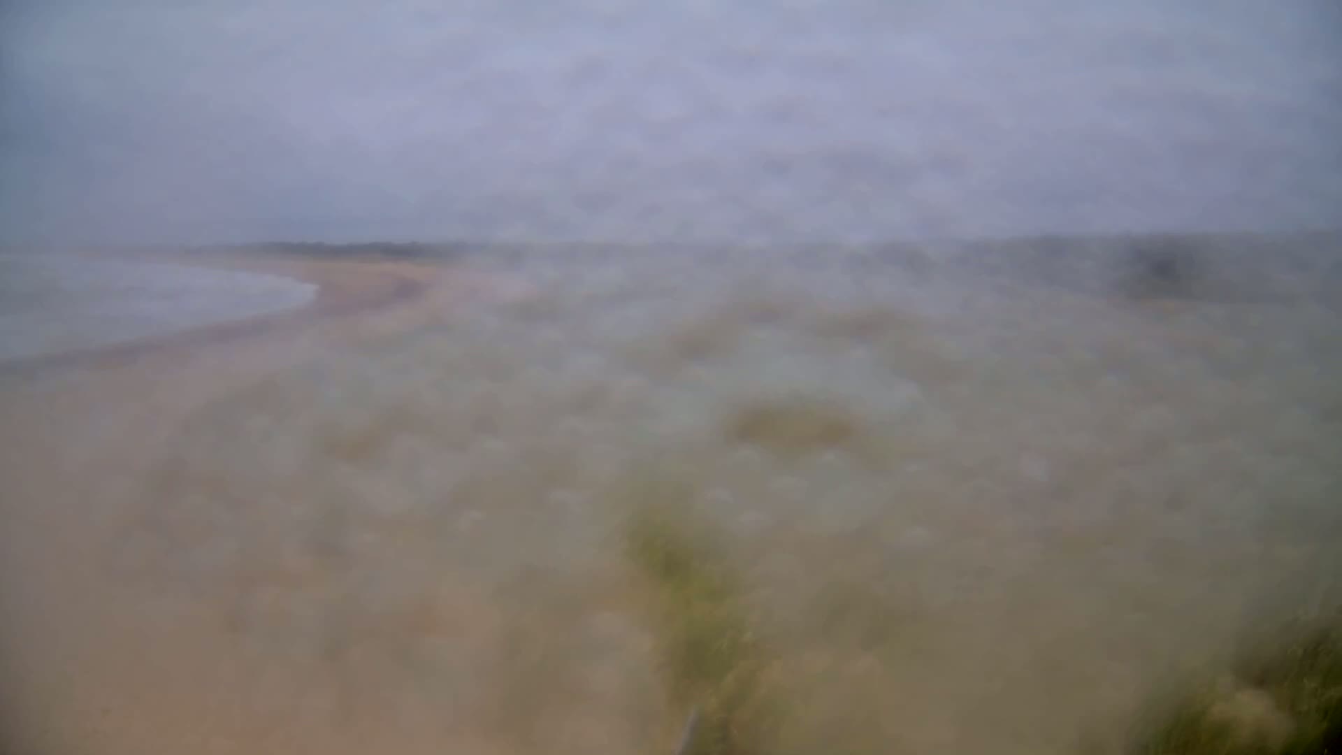 A blurry image shows a sandy beach and calm ocean under an overcast sky.
