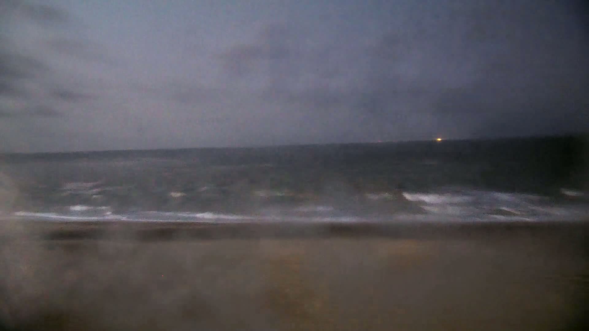 A dark, overcast sky hangs over a beach with choppy waves rolling onto the shore.