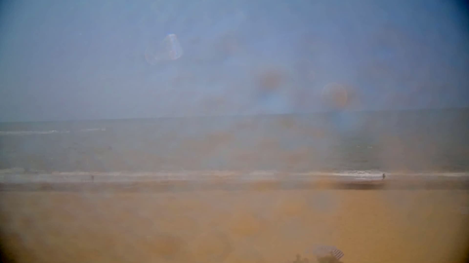 A hazy view of a beach and ocean, with a few people visible in the distance.