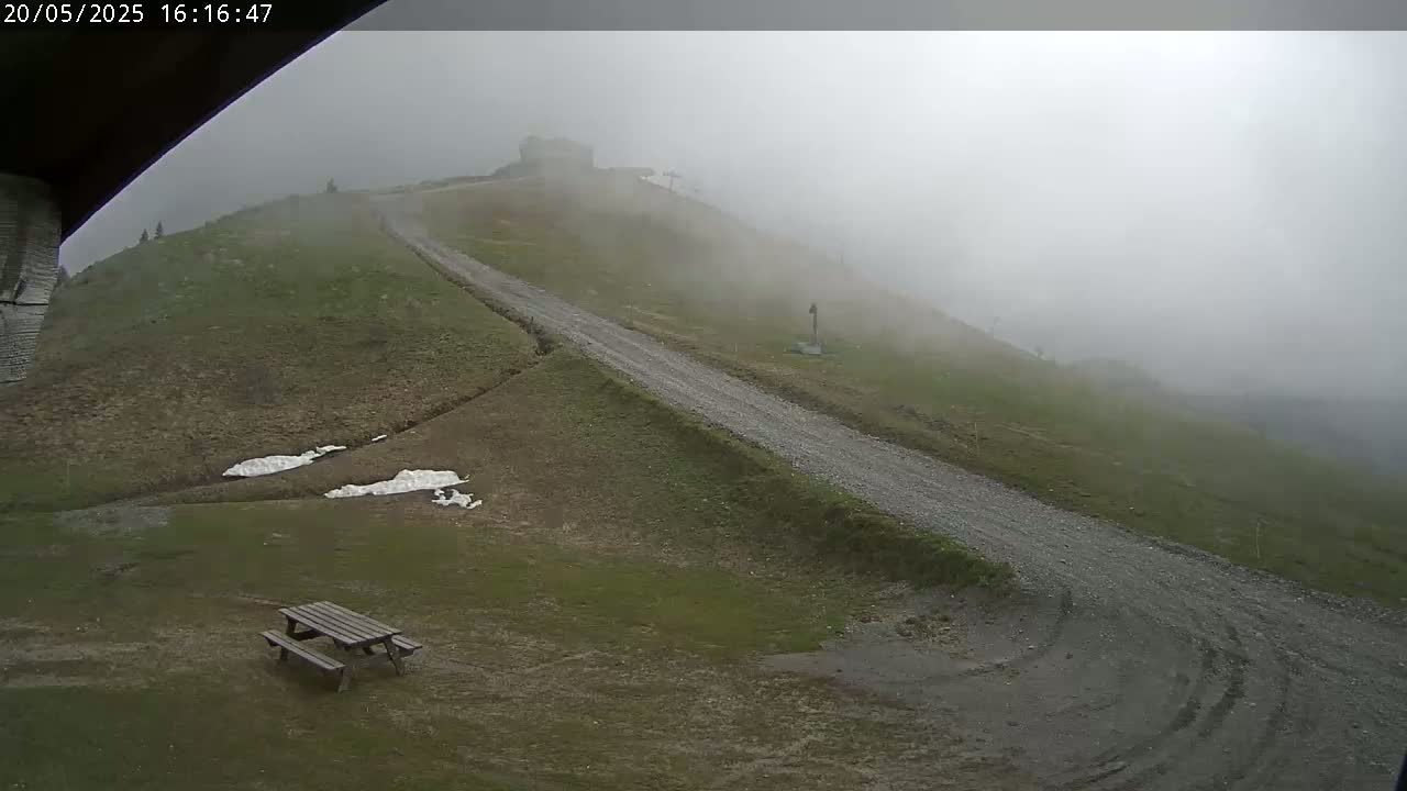 A gravel road winds uphill toward a foggy mountaintop, past a picnic table and small patches of snow.