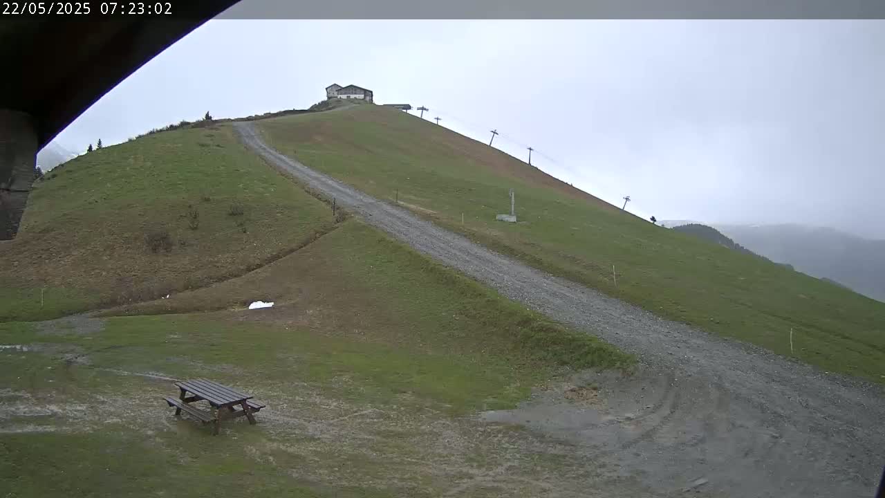 A gravel road winds up a grassy hillside toward a small building and a ski lift under an overcast sky.