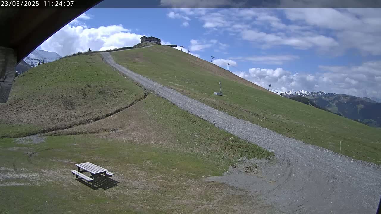 A gravel road winds up a grassy hillside toward a small building and ski lift under a partly cloudy sky.