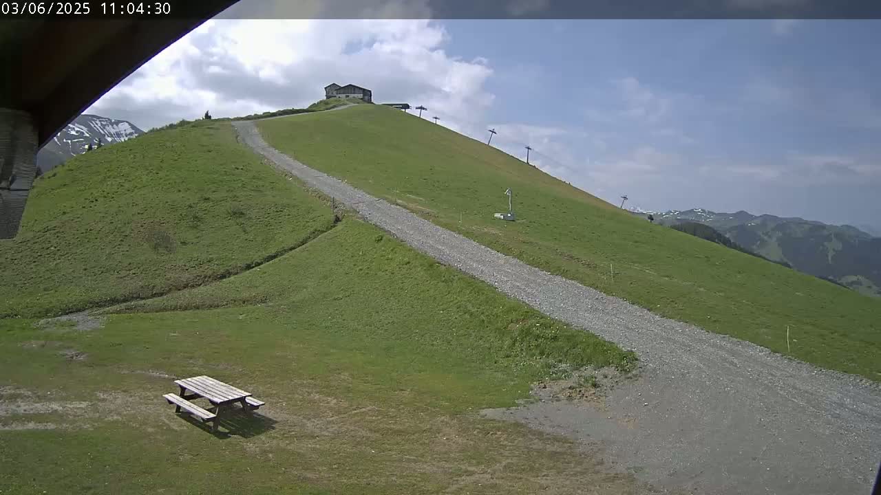 A gravel path winds up a grassy hill towards a small building and ski lift under a partly cloudy sky.