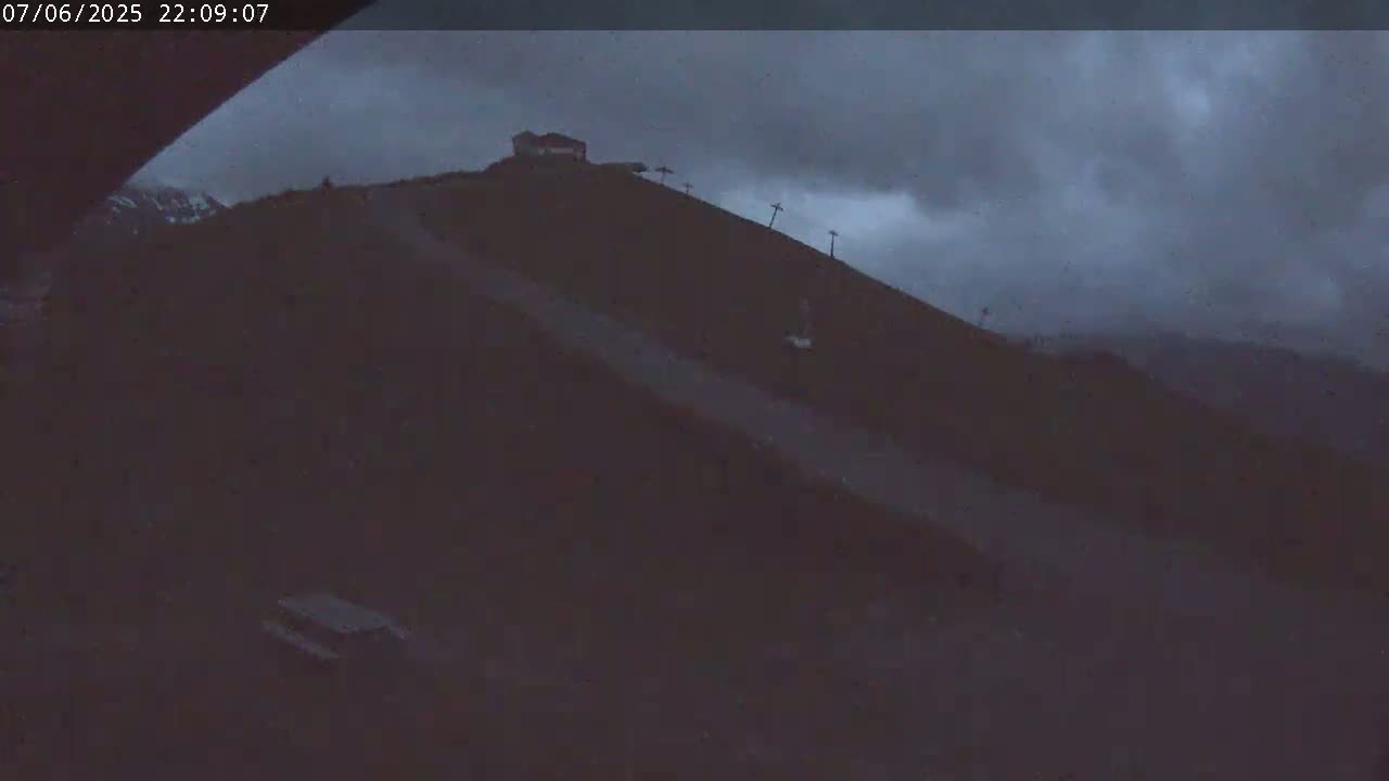 A dark, overcast sky looms over a hilltop with a small building and ski lift infrastructure.