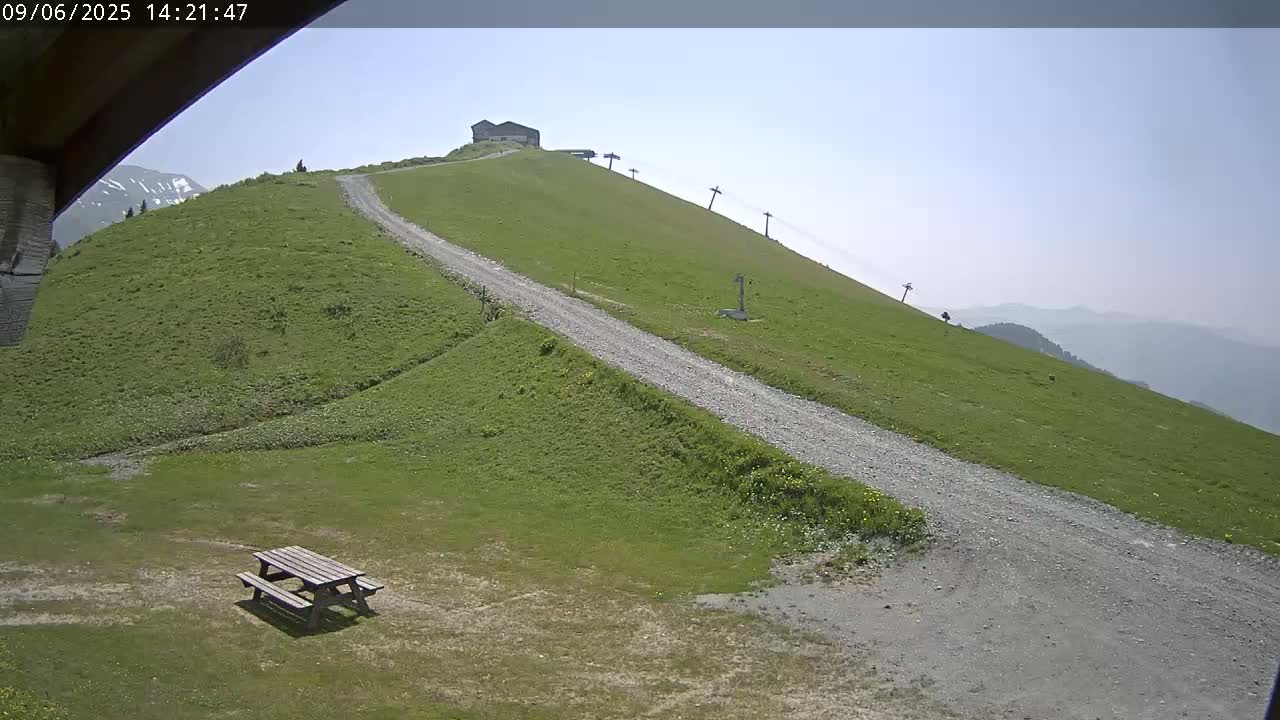 A gravel road winds up a grassy hillside under a clear, sunny sky, passing a picnic table and a small building near the top.