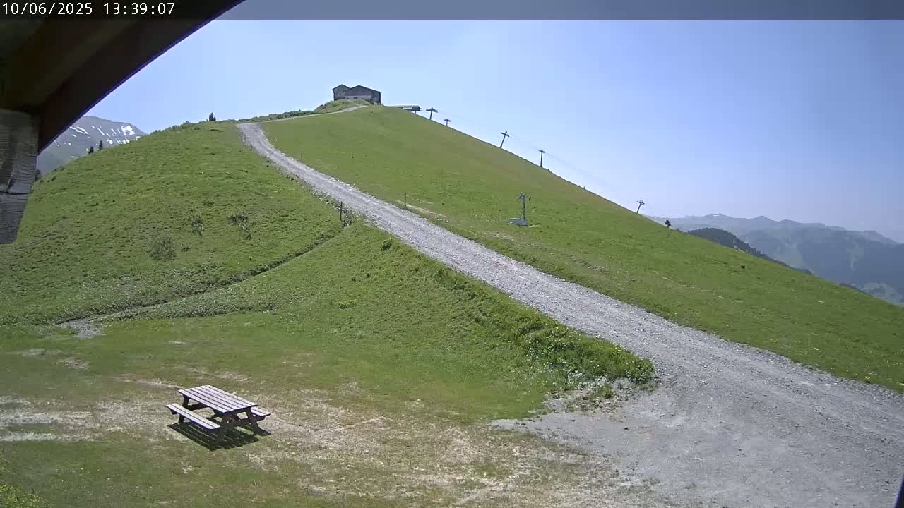 A gravel road winds up a grassy hill towards a small building and ski lift under a clear blue sky.