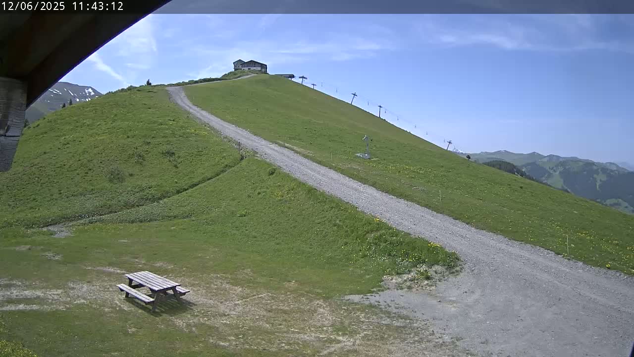 A grassy hillside with a gravel road leading to a small building and a chairlift, under a mostly clear blue sky.