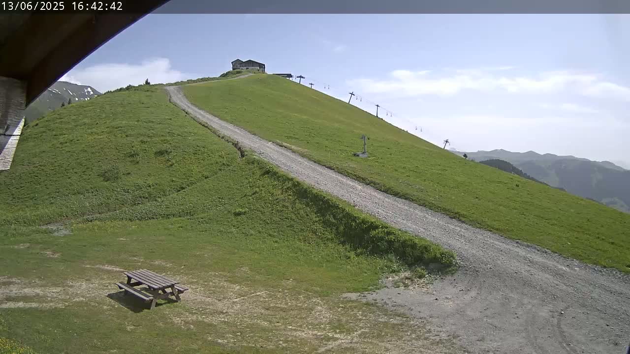 A grassy hillside with a gravel road leading to a small building and chairlift, under a mostly clear sky.