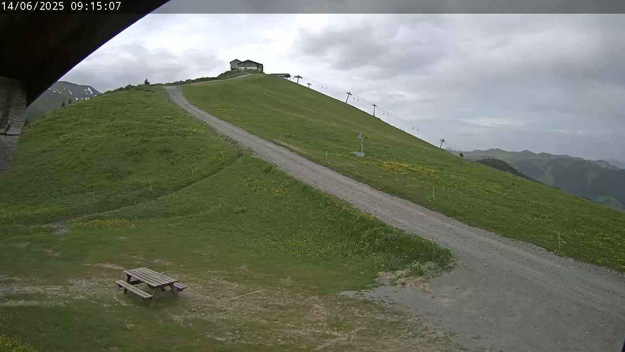 A gravel road winds up a grassy hill towards a small building and a chairlift under a cloudy sky.