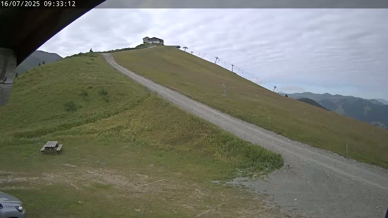 A gravel road winds up a grassy hill towards a small building and a chairlift under an overcast sky.