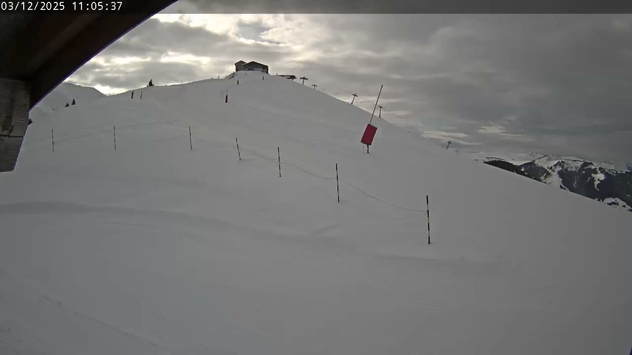 A snow-covered ski slope with a building and ski lifts visible at the summit is pictured under a partly cloudy sky.