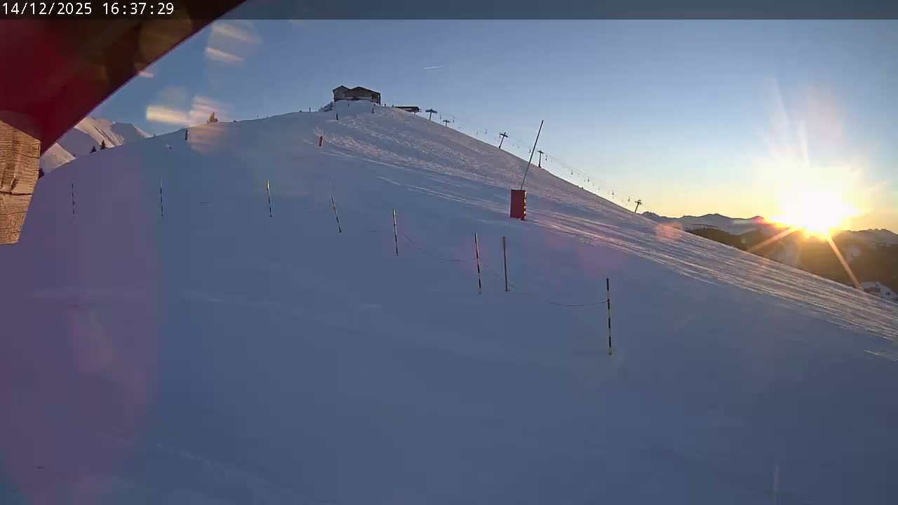 A snow-covered ski slope with a building and ski lifts visible at the summit is pictured under a partly cloudy sky.