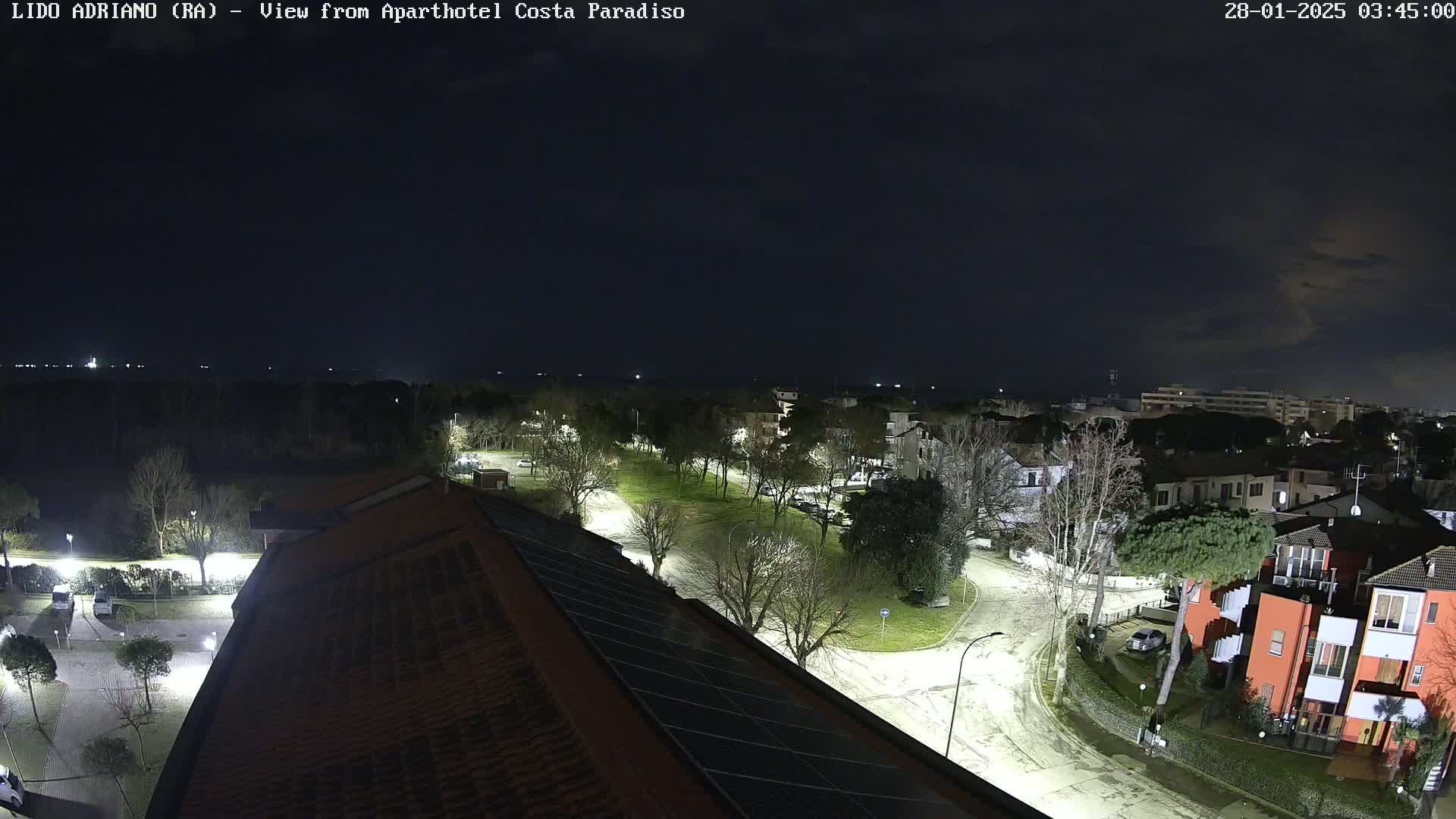A nighttime aerial view of a residential area with streets, trees, and buildings, illuminated by streetlights under a dark, mostly clear sky.