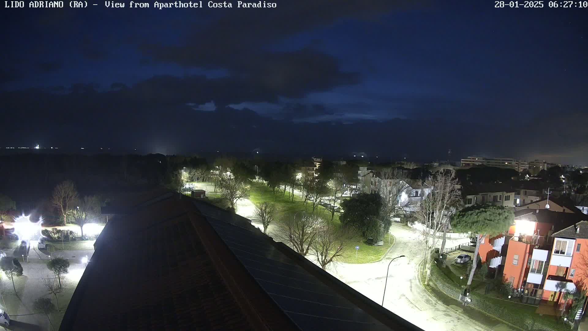 A nighttime view of a residential area with illuminated streets and buildings under a partly cloudy sky.