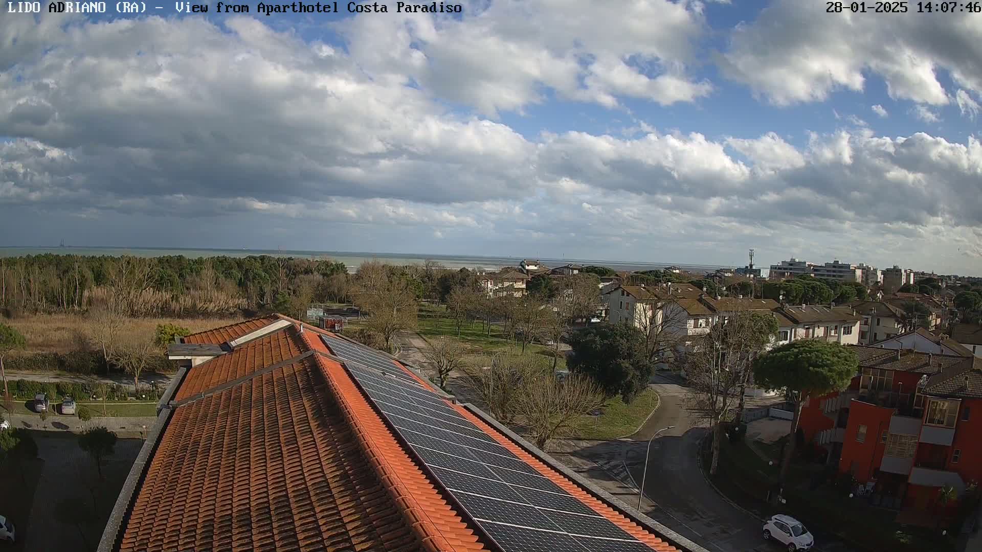 A partly cloudy sky overlooks a coastal town with a residential area and a building rooftop equipped with solar panels.