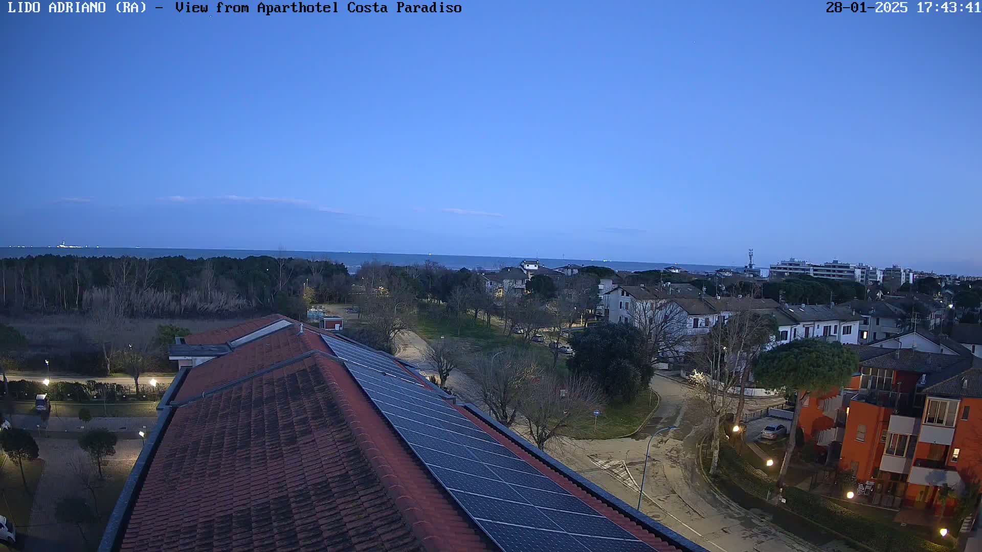A coastal residential area is visible at dusk under a clear, twilight sky, seen from a rooftop with solar panels.