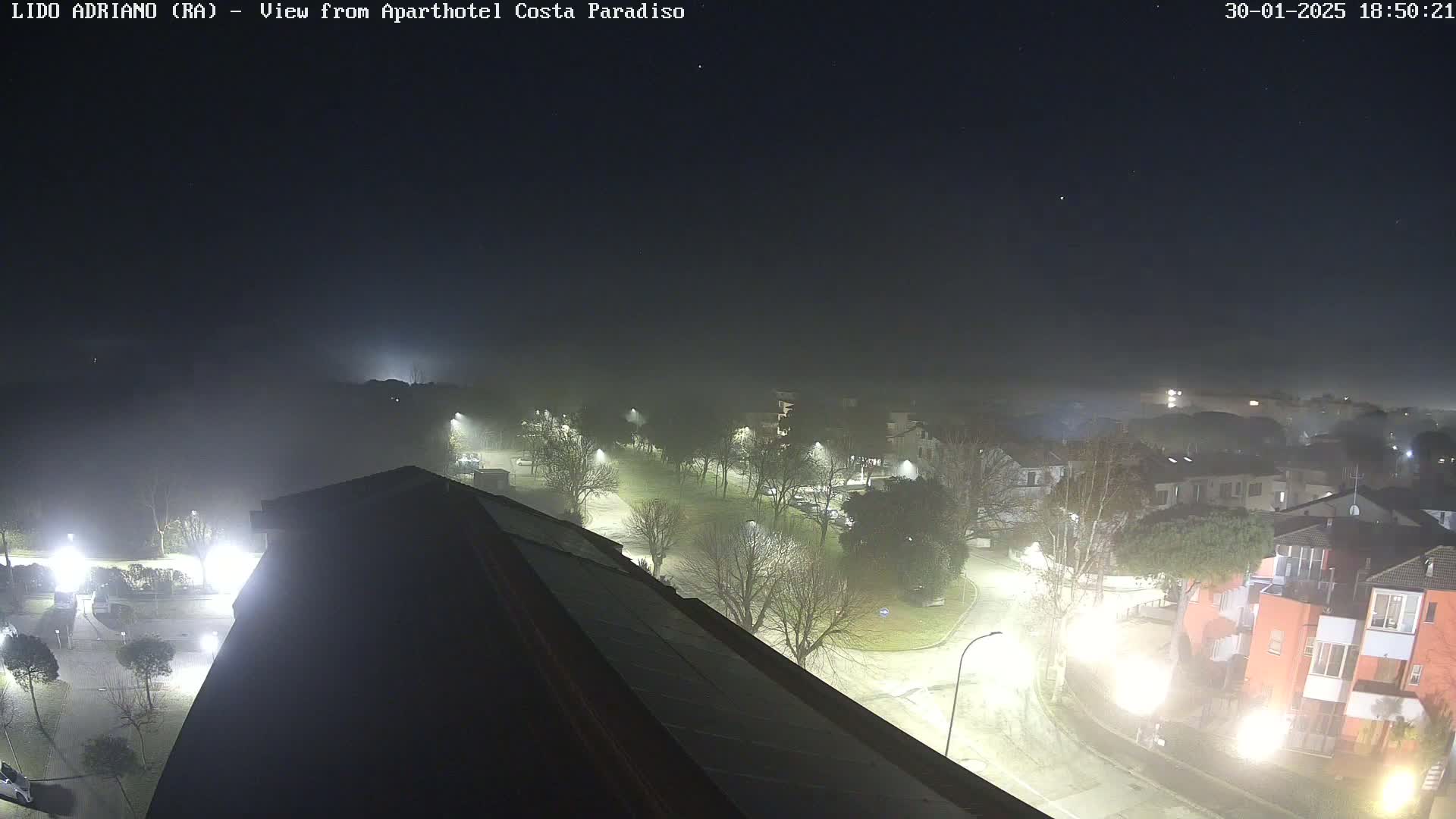 A nighttime, foggy view of a residential area with streetlights illuminating roads and buildings.