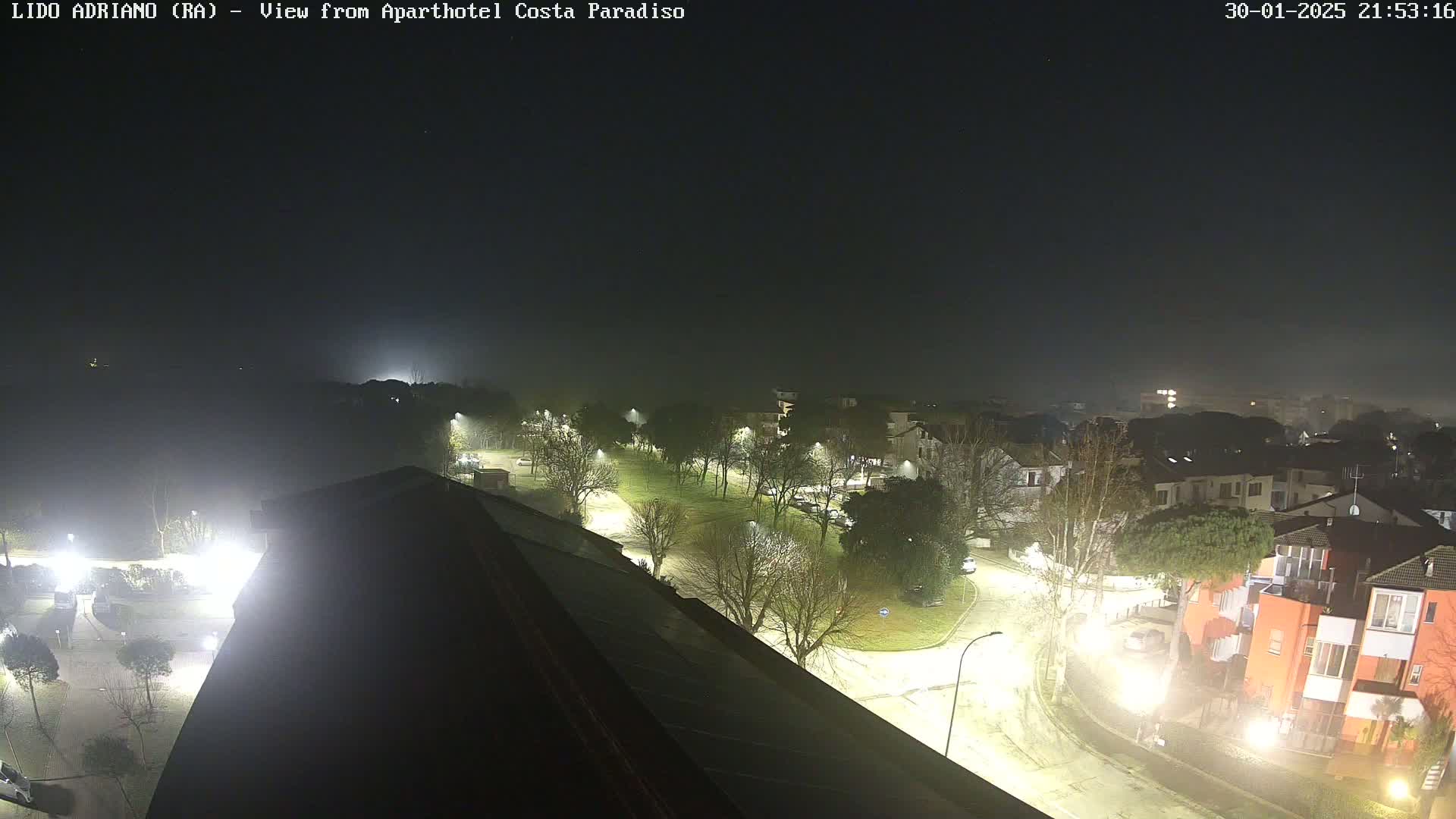 A nighttime, foggy view of a residential area with illuminated streets and buildings.