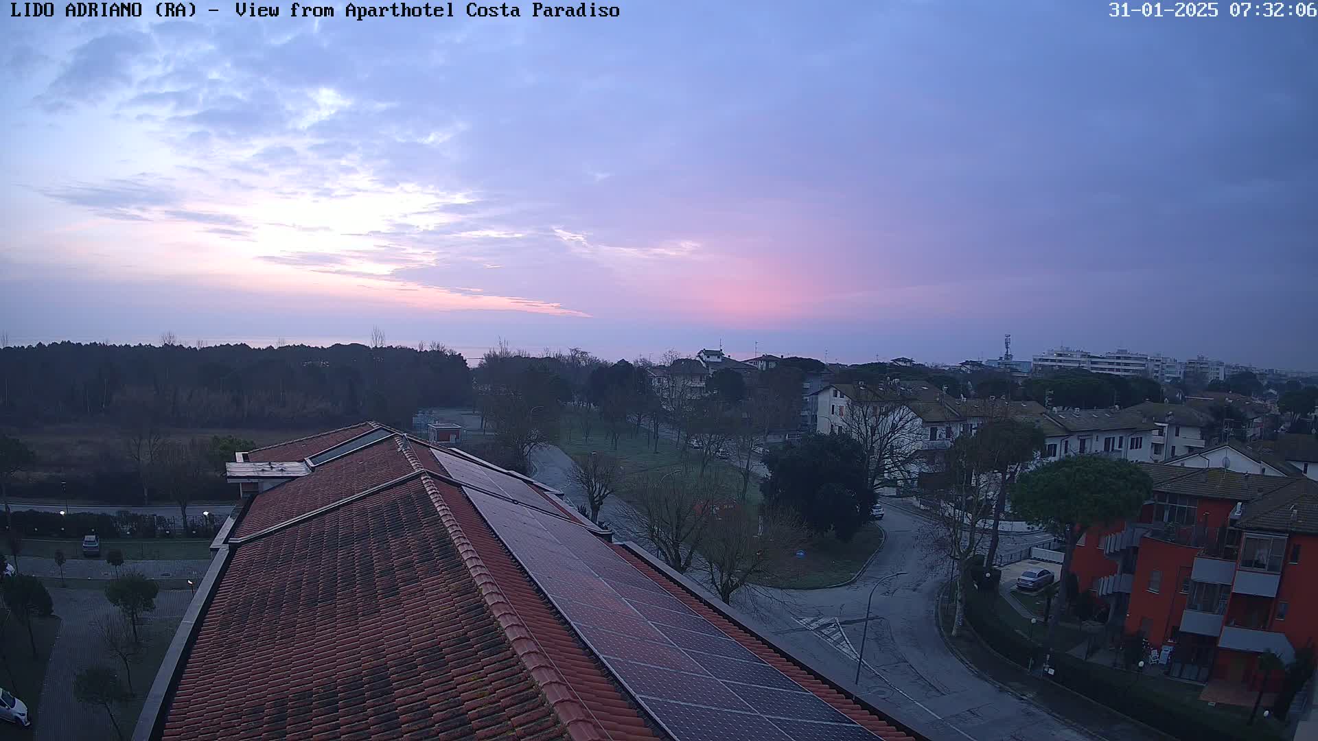 A rooftop view of a residential area near a calm body of water under a dusky pink and purple sunrise sky.