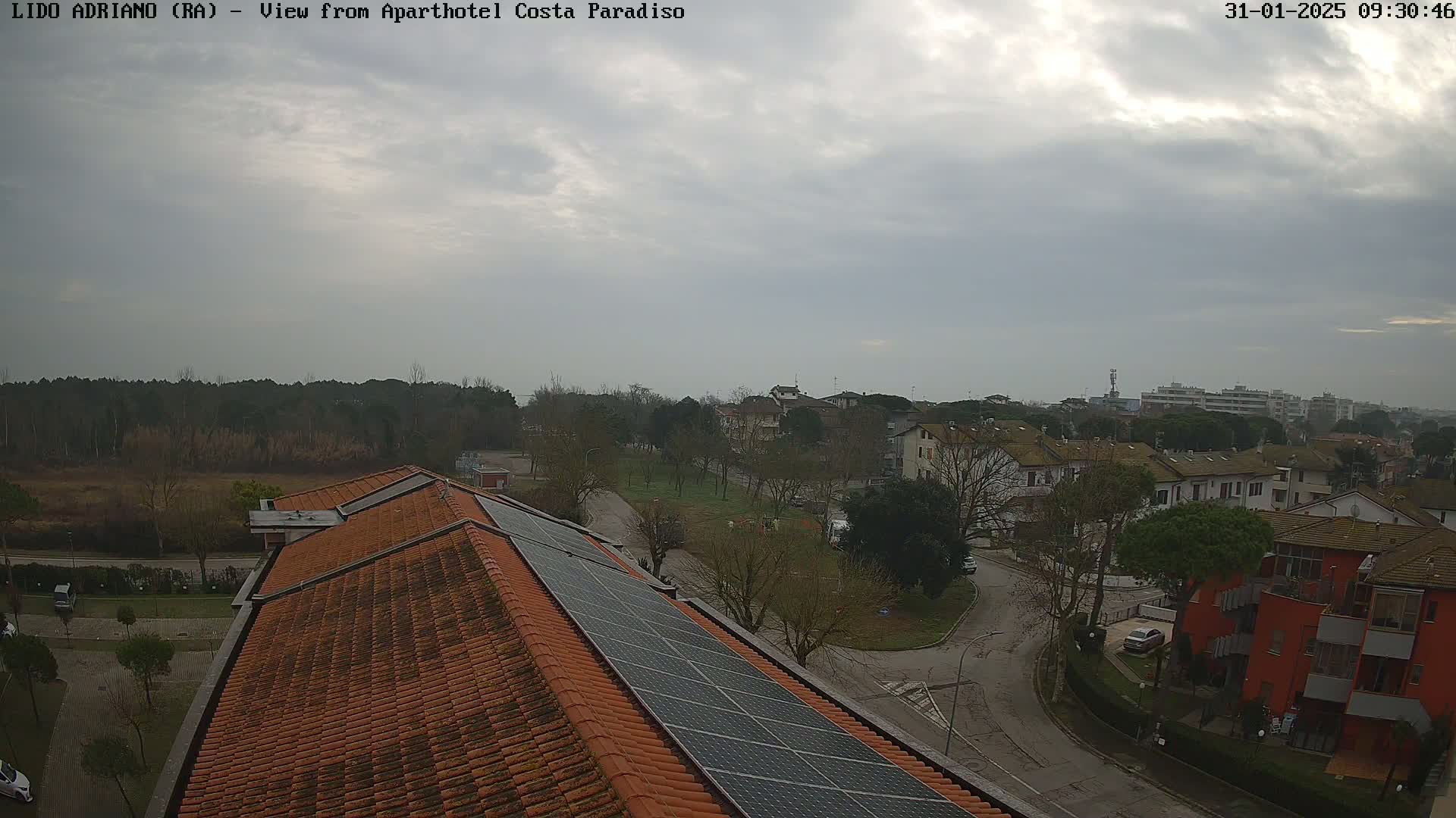 A rooftop with solar panels overlooks a residential area on an overcast day.