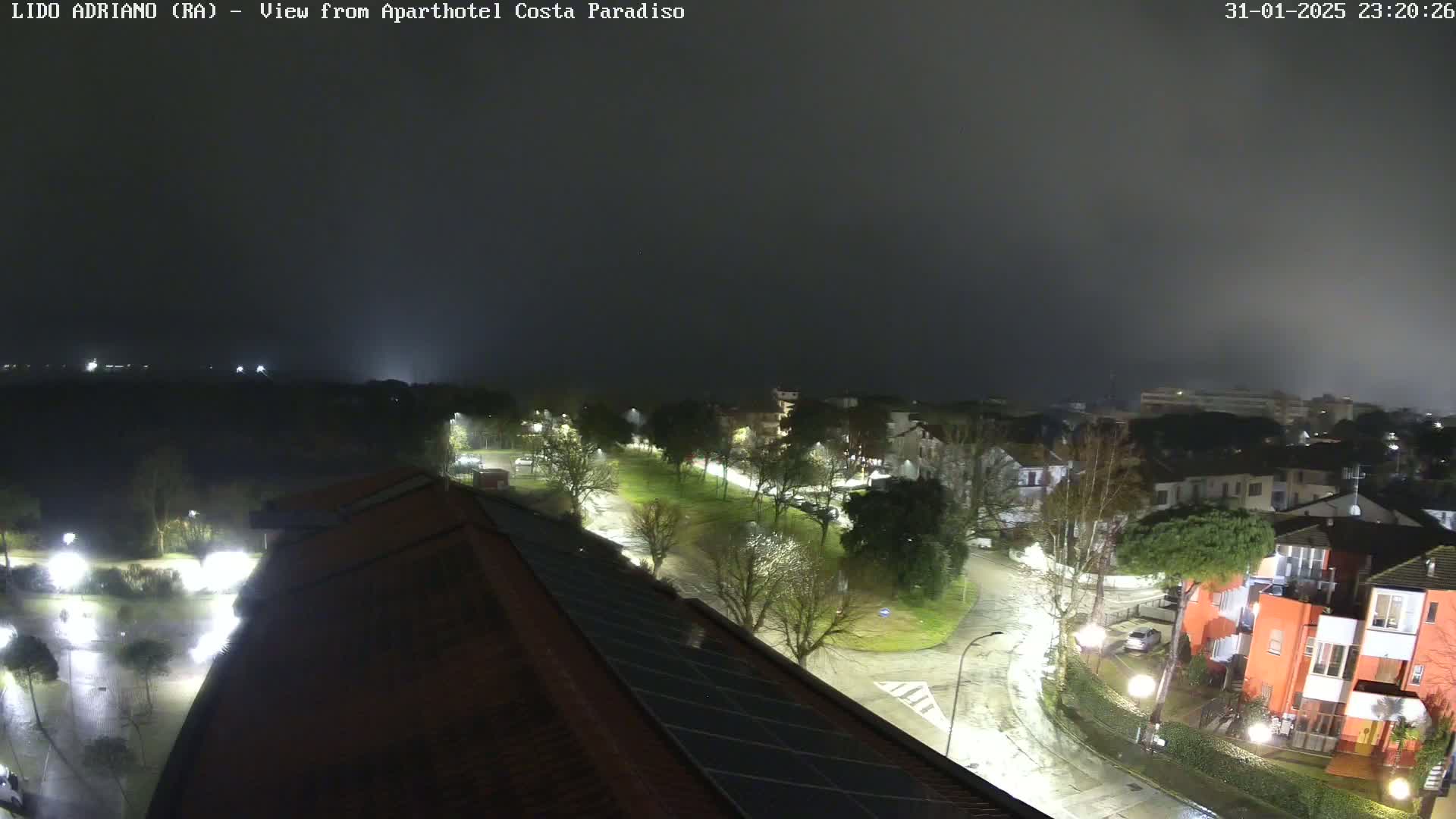 A nighttime view of rain-slicked streets and buildings under a foggy sky.
