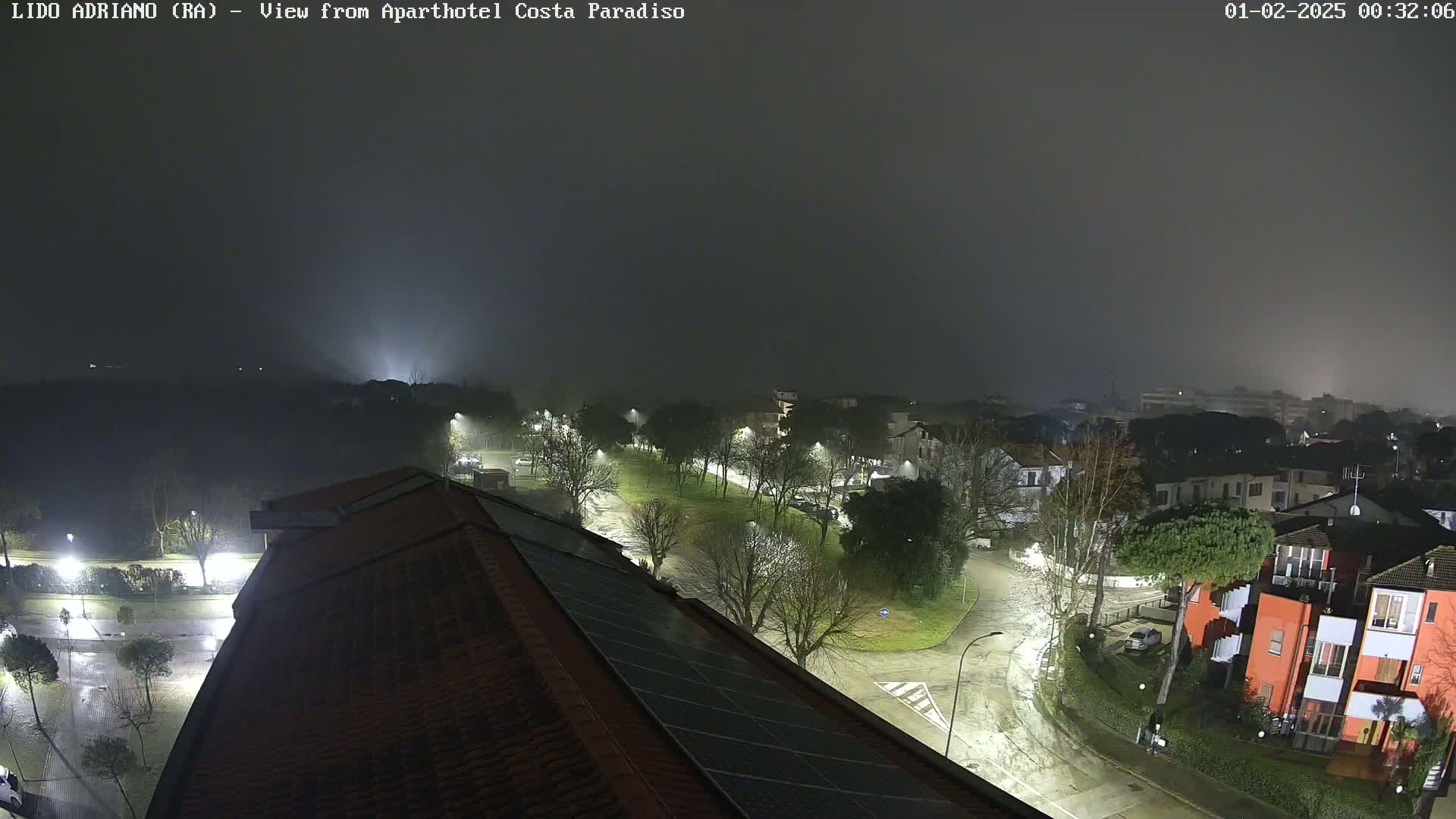 A nighttime view of a rain-slicked town, shrouded in fog, shows streetlights illuminating roads and buildings.