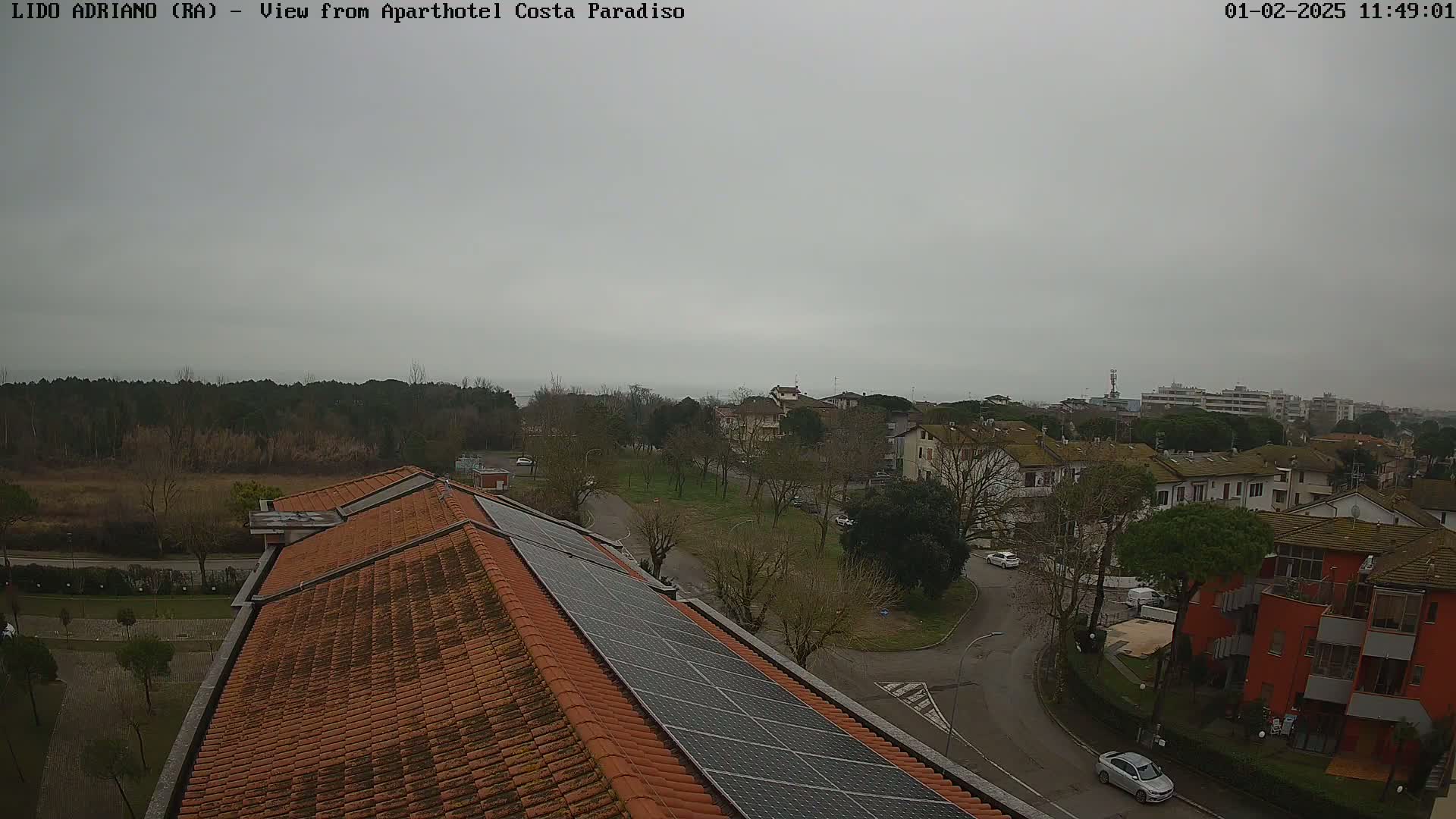 A view from a rooftop with solar panels shows a residential area under an overcast sky.