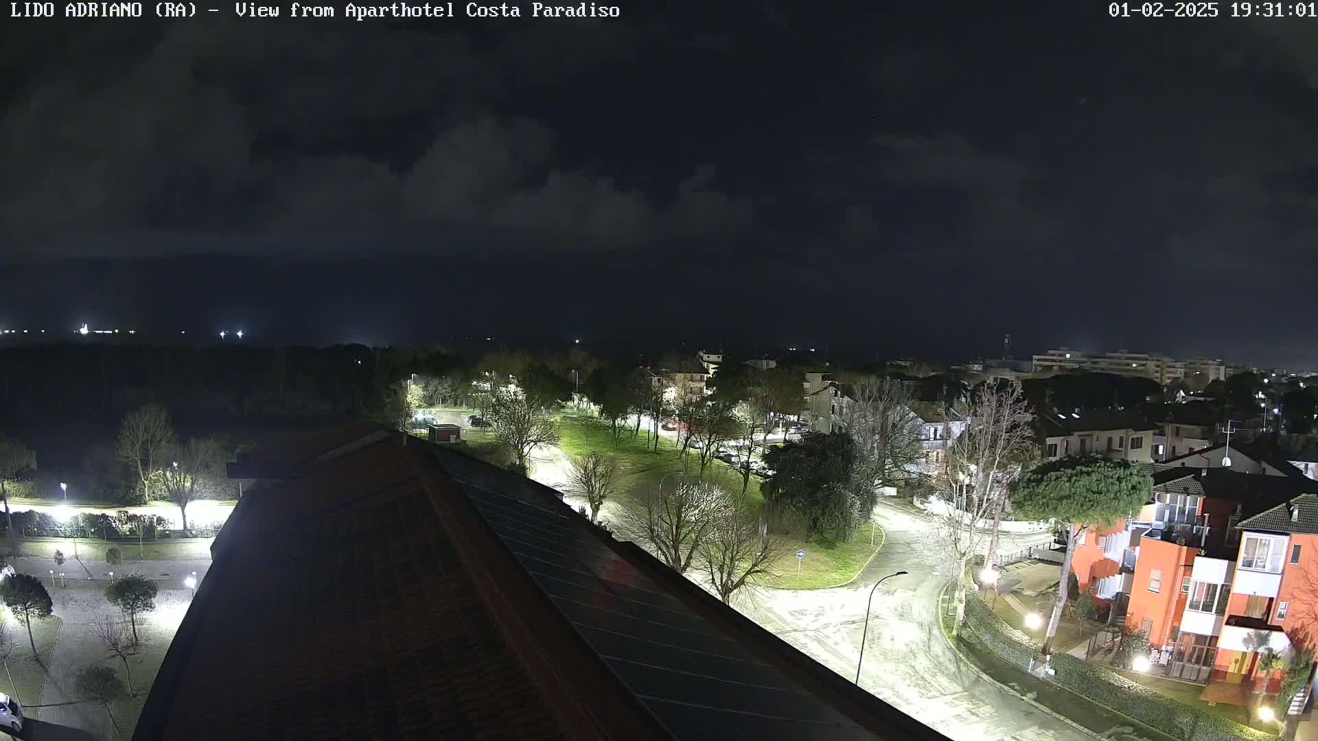 A nighttime view of a residential area with a park and roads, under a cloudy sky.