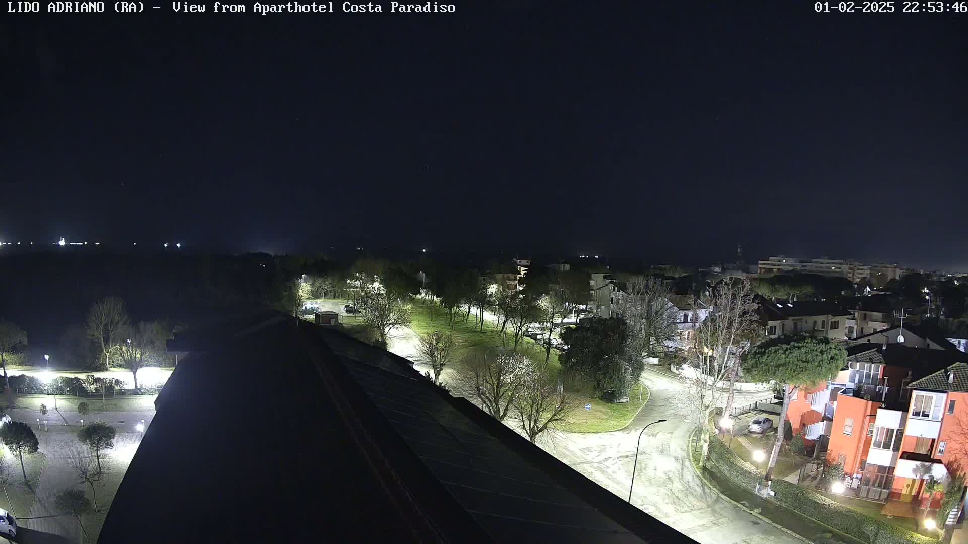 A nighttime aerial view of a residential area with a park, illuminated streets, and some snow or ice on the ground.