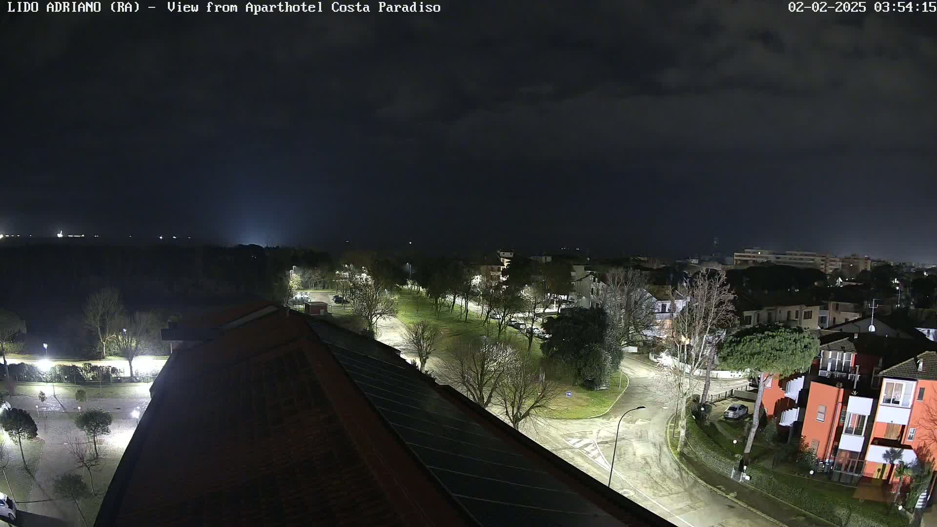 A nighttime view of a residential area with streets and buildings, under a cloudy sky.