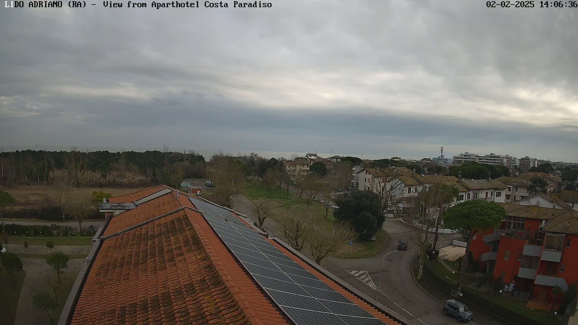 An overcast day reveals a view of a coastal town with a red building, residential homes, and a large solar panel array on a terracotta roof.