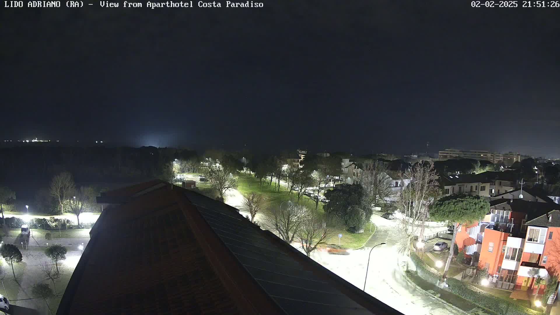 A nighttime view of a residential area with a park, illuminated by streetlights, under a dark, clear sky.