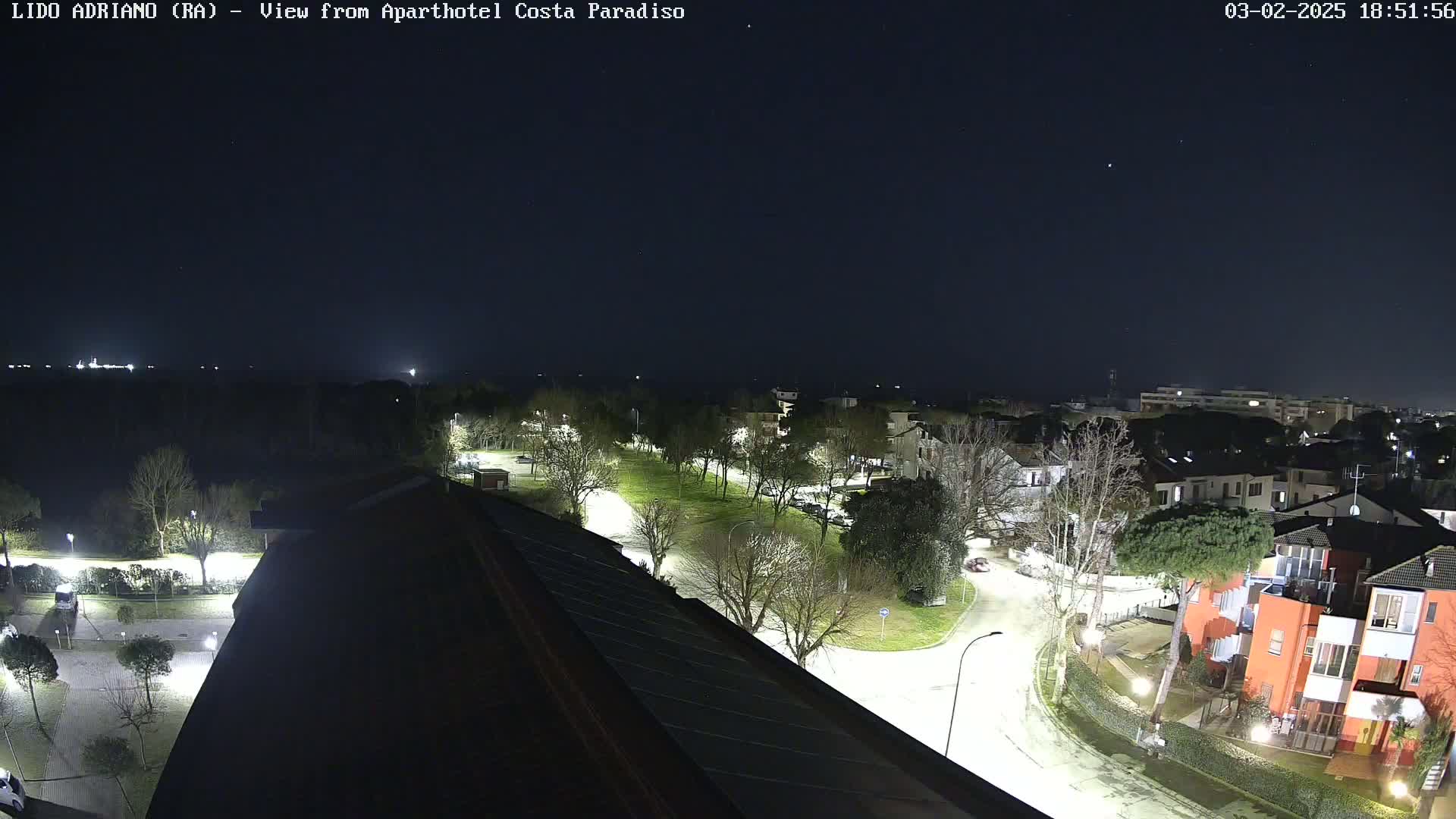A nighttime view of a residential area with streets lit by lamps, under a clear, dark sky.