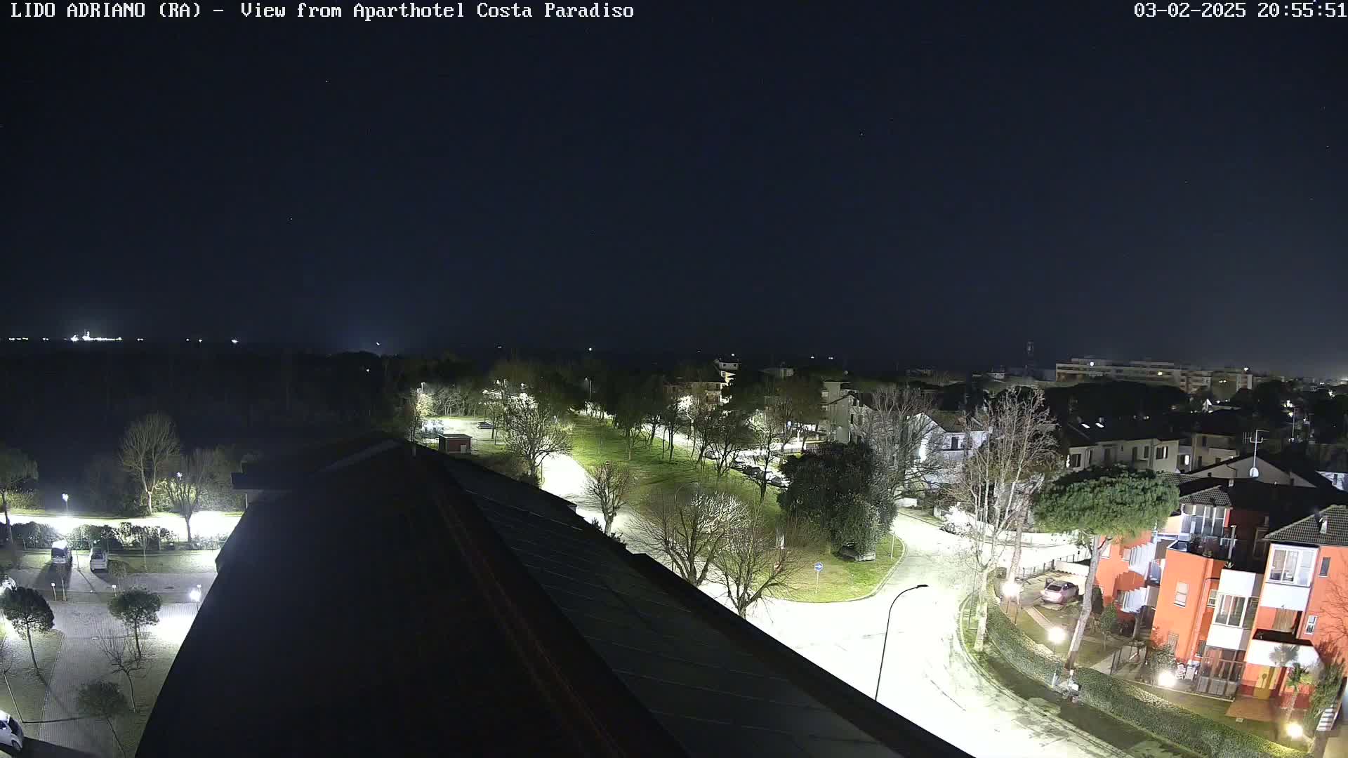 A nighttime, overhead view of a residential area with illuminated streets, trees, and buildings under a clear, dark sky.