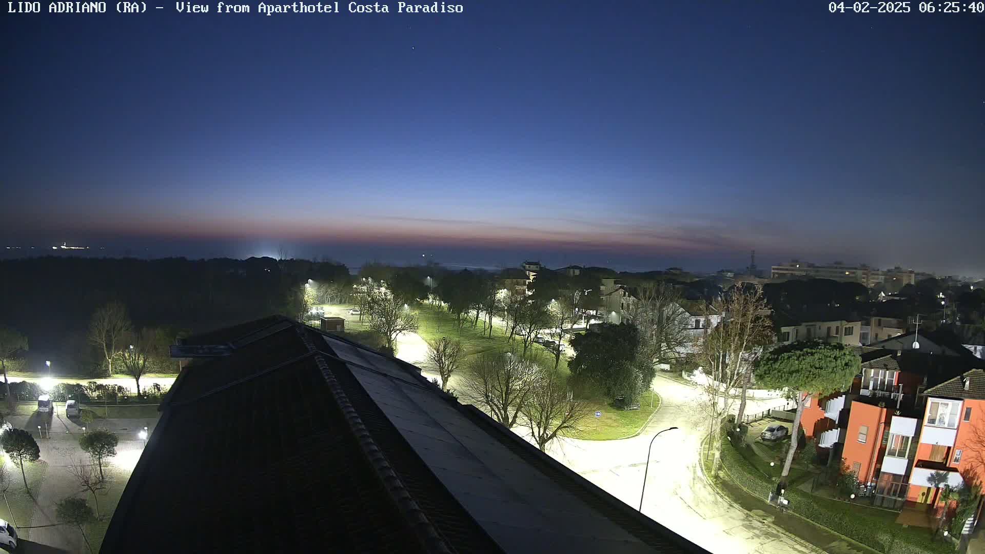 A nighttime view of a residential area near a coastline, with the sky showing the transition from dusk to night.