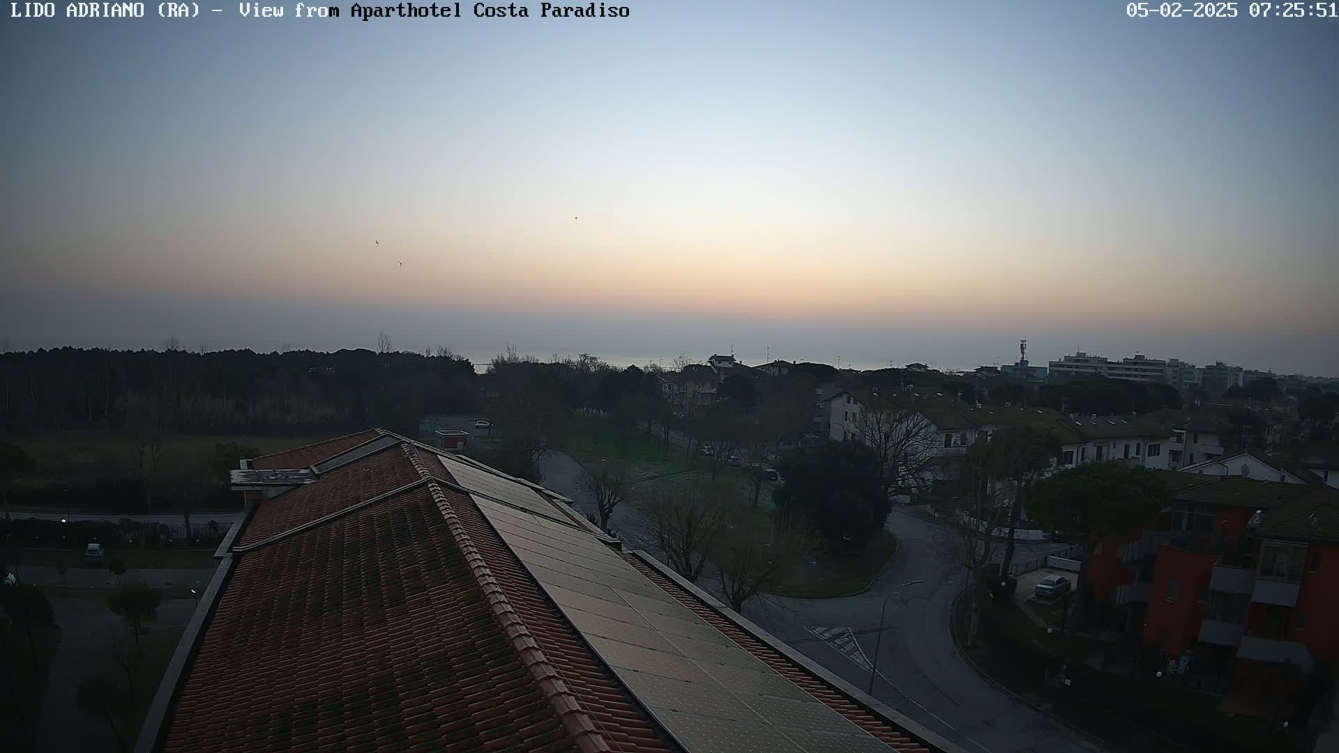 A view from a rooftop shows a residential area with a calm sea in the distance under a twilight sky.