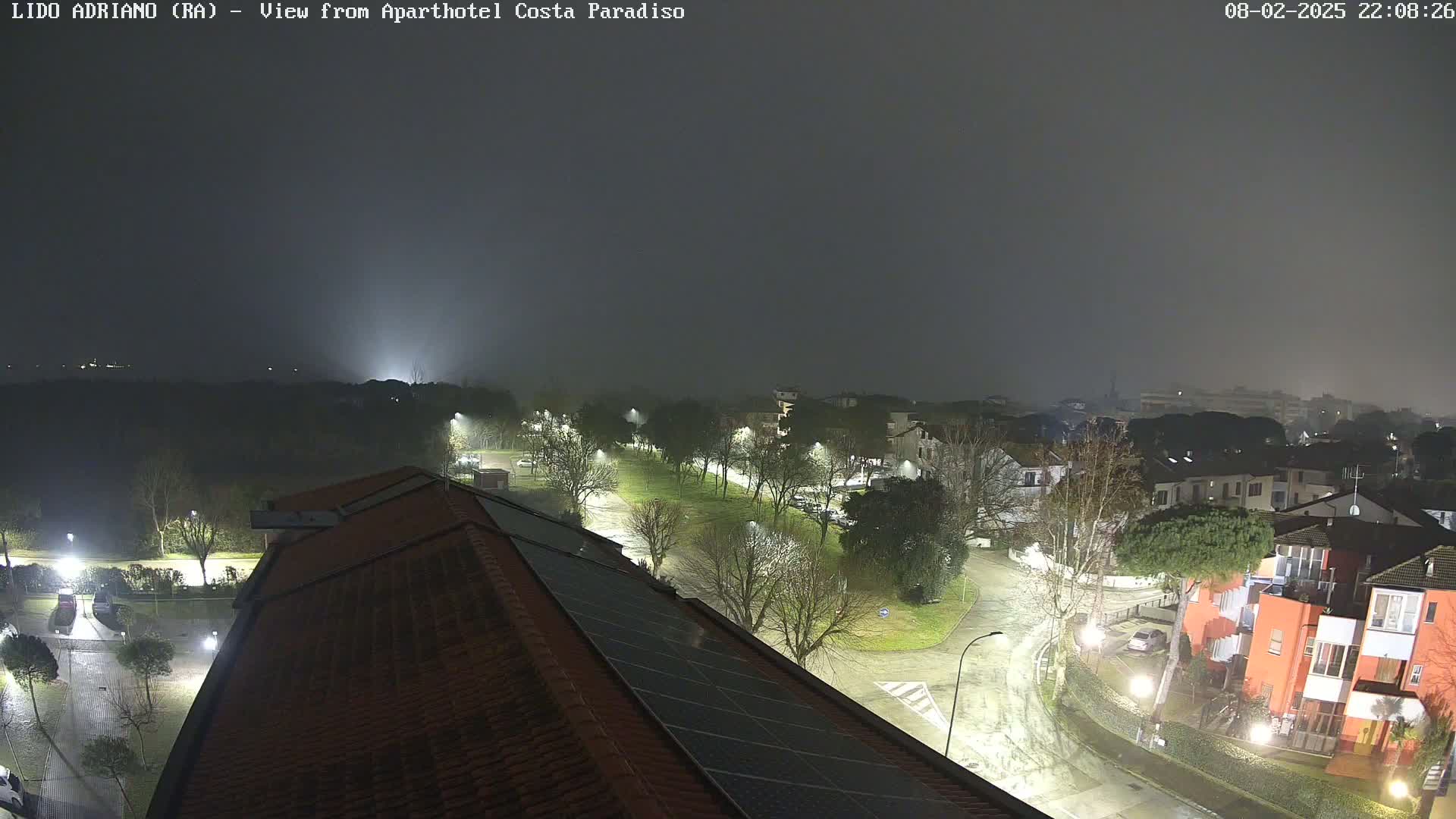 A nighttime view of a residential area shrouded in fog, with streetlights illuminating wet roads and buildings.