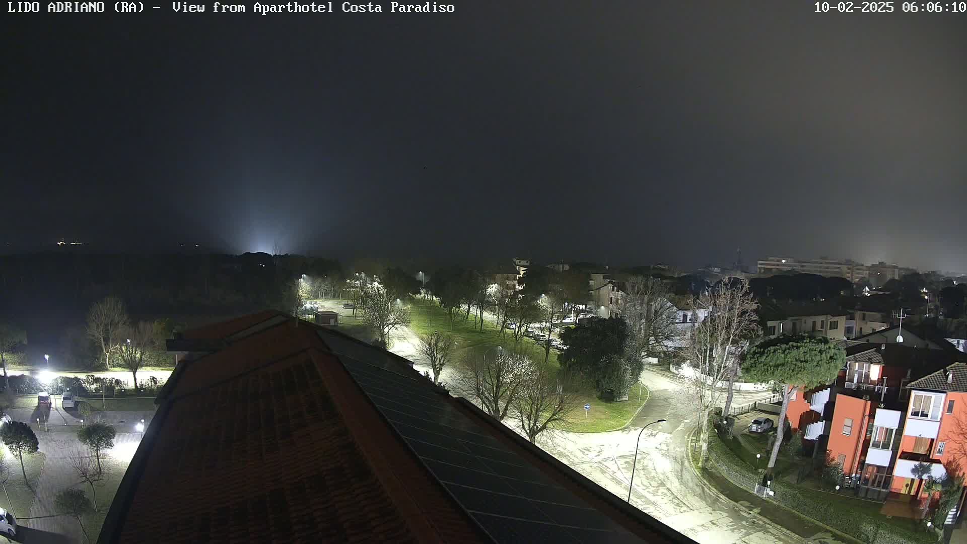 A nighttime, foggy view of a residential area with roads, trees, and buildings illuminated by streetlights.